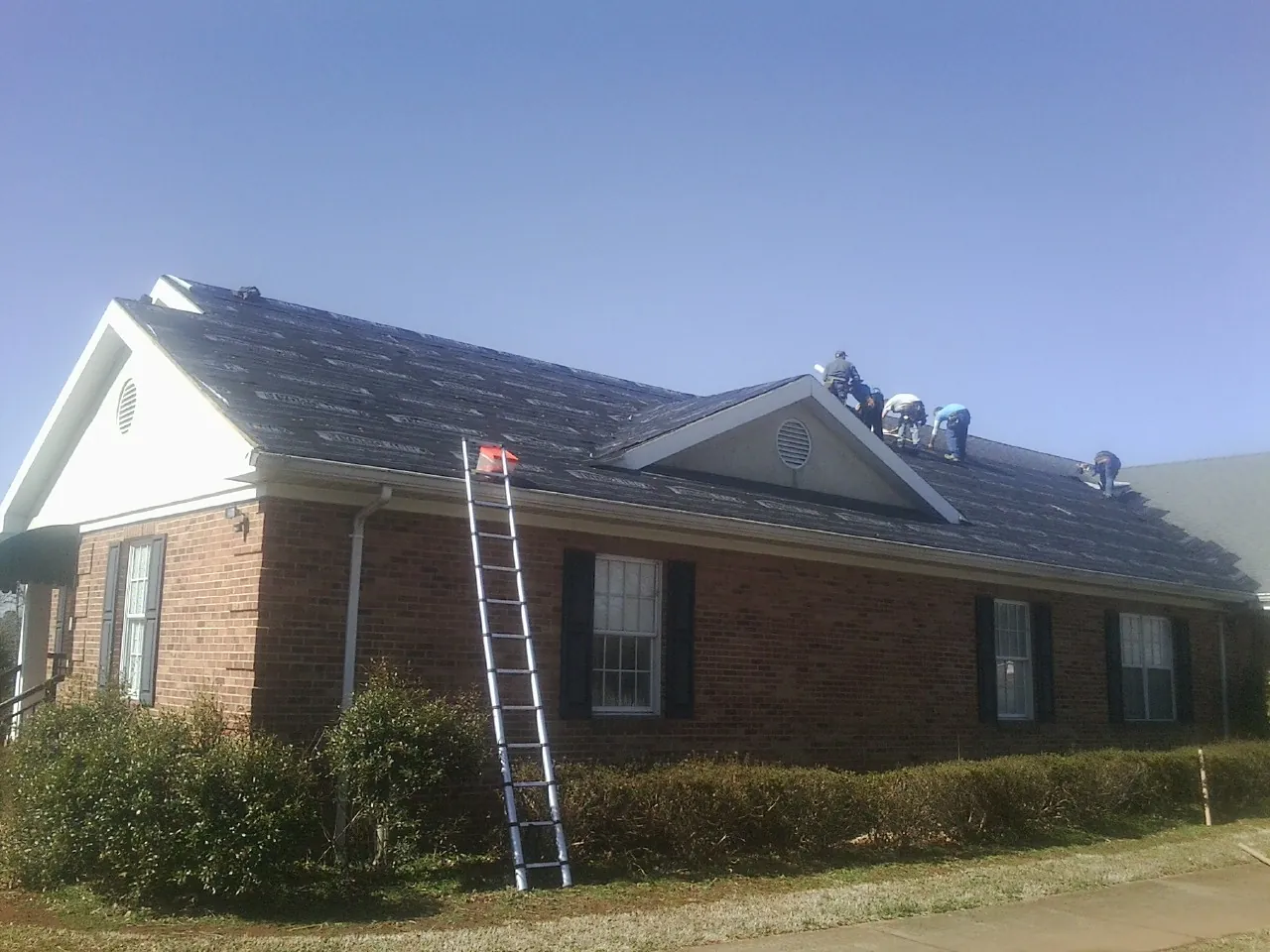 Crew tearing shingles off a brick ranch roof with a ladder set — Emergency Roof Repair work by our crew in Edgar