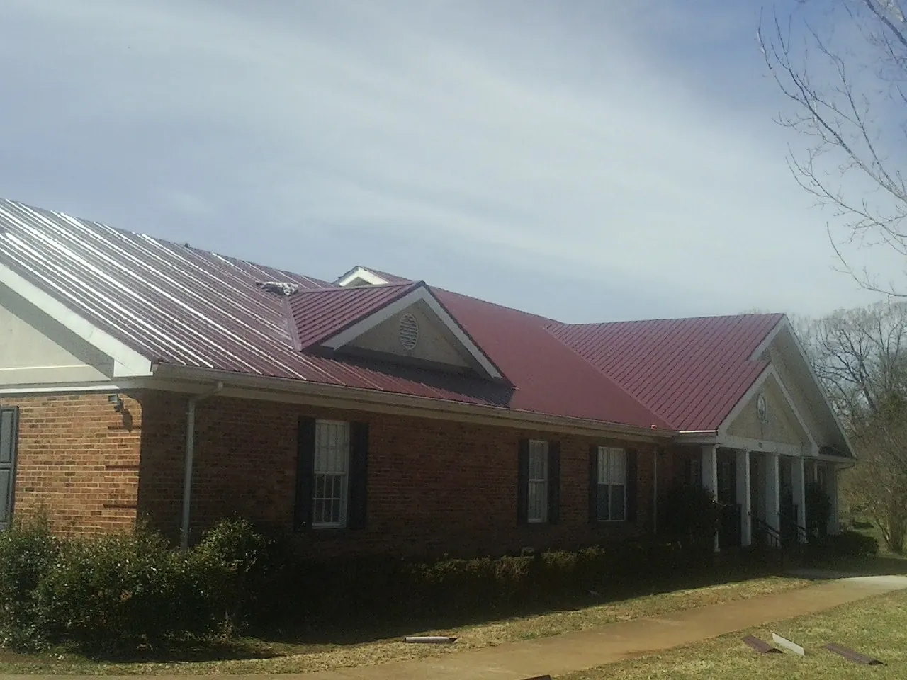 Red metal roof with gabled entries on a long brick building, from a Hail Damage Roof Repair job in Edgar